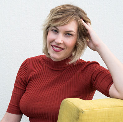 lauren atkinson in red smiling and sitting on a yellow chair